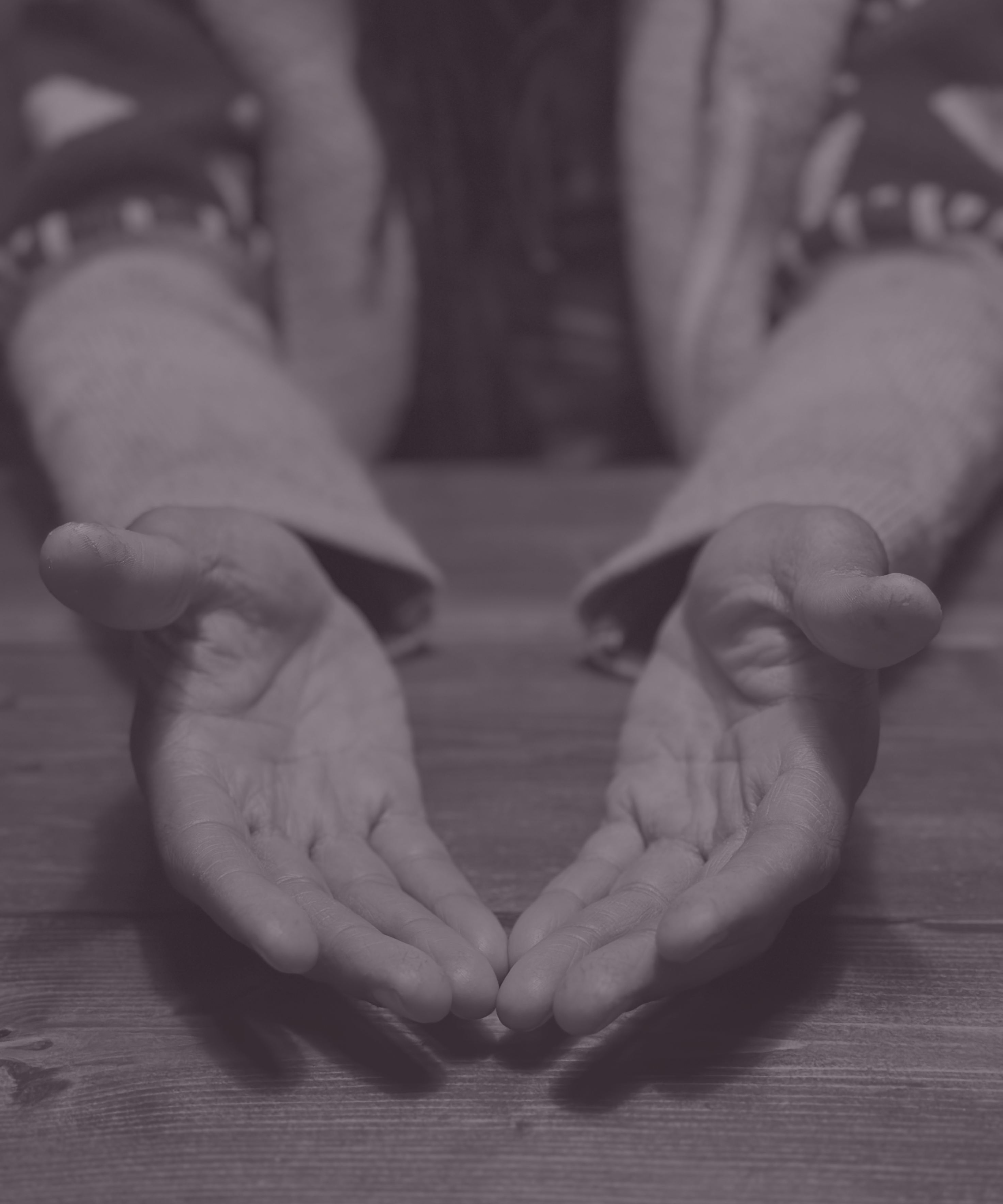 A person with dreadlocks and a masculine, sweatered chest extends their arms; two large, calloused brown hands comfortingly welcome the viewer.